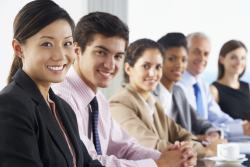 Line Of Business People Listening To Presentation Seated At Glass Boardroom Table